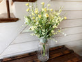 Mason jar with yellow flowers on a wooden surface against a white wall.