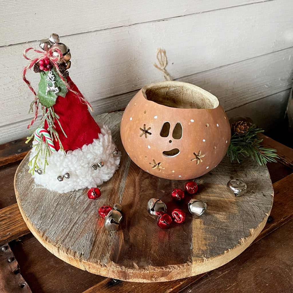 Decorative lantern with face, small figurine, and jingle bells on a wooden surface.