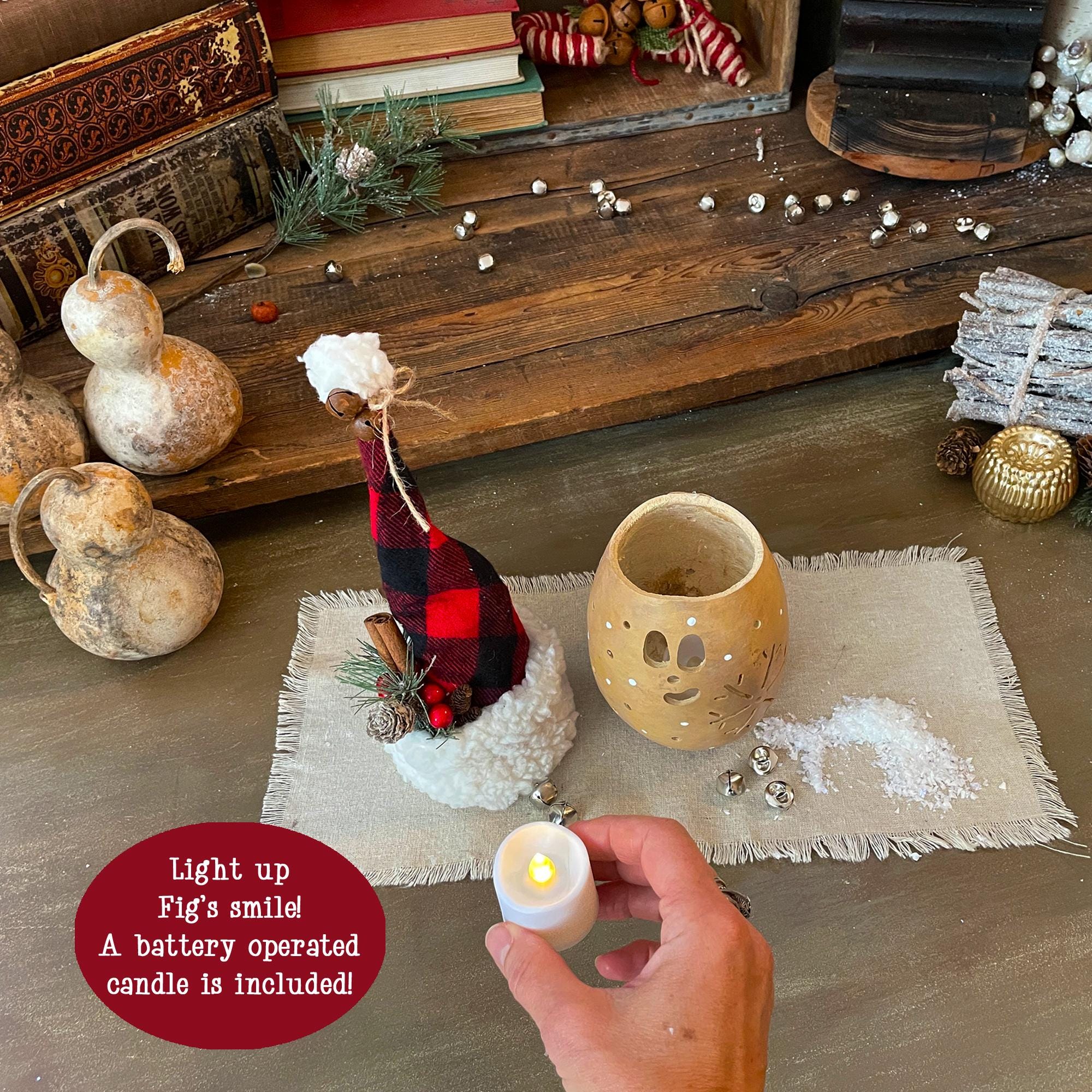 Decorative setup with a small candle, plaid figurine, and lantern on a wooden surface.