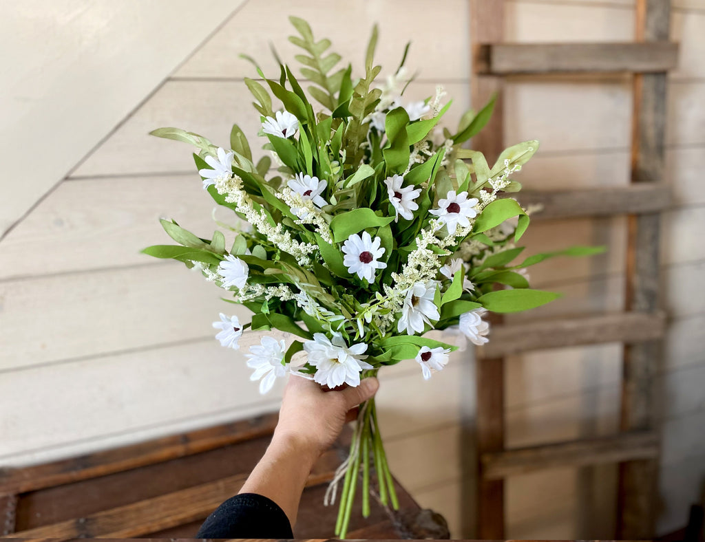Bouquet of white flowers with green leaves held by a hand against a wooden background