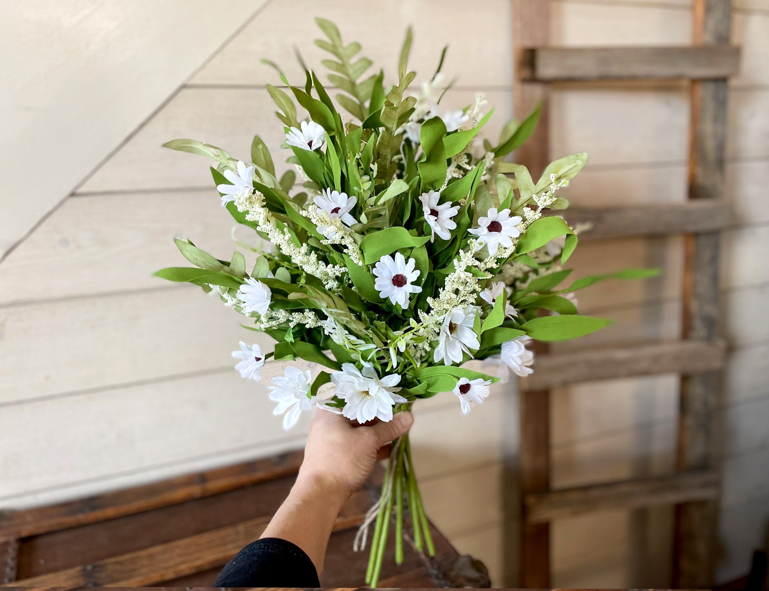Bouquet of white flowers with green leaves held by a hand against a wooden background