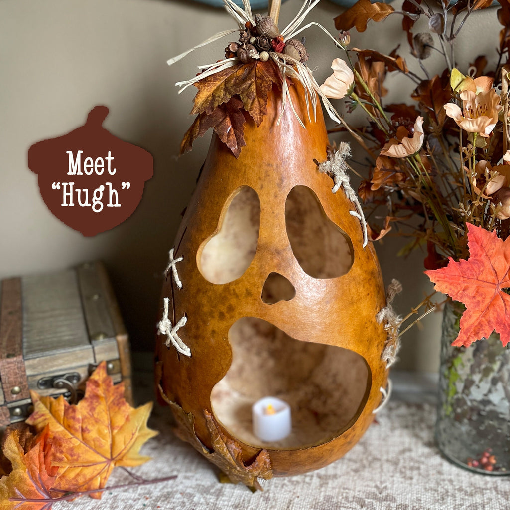 Decorative gourd with cut-out shapes and a candle inside, surrounded by autumn leaves and flowers.