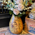 Decorative vase with floral design and text, placed on a surface with a wooden box in the background.
