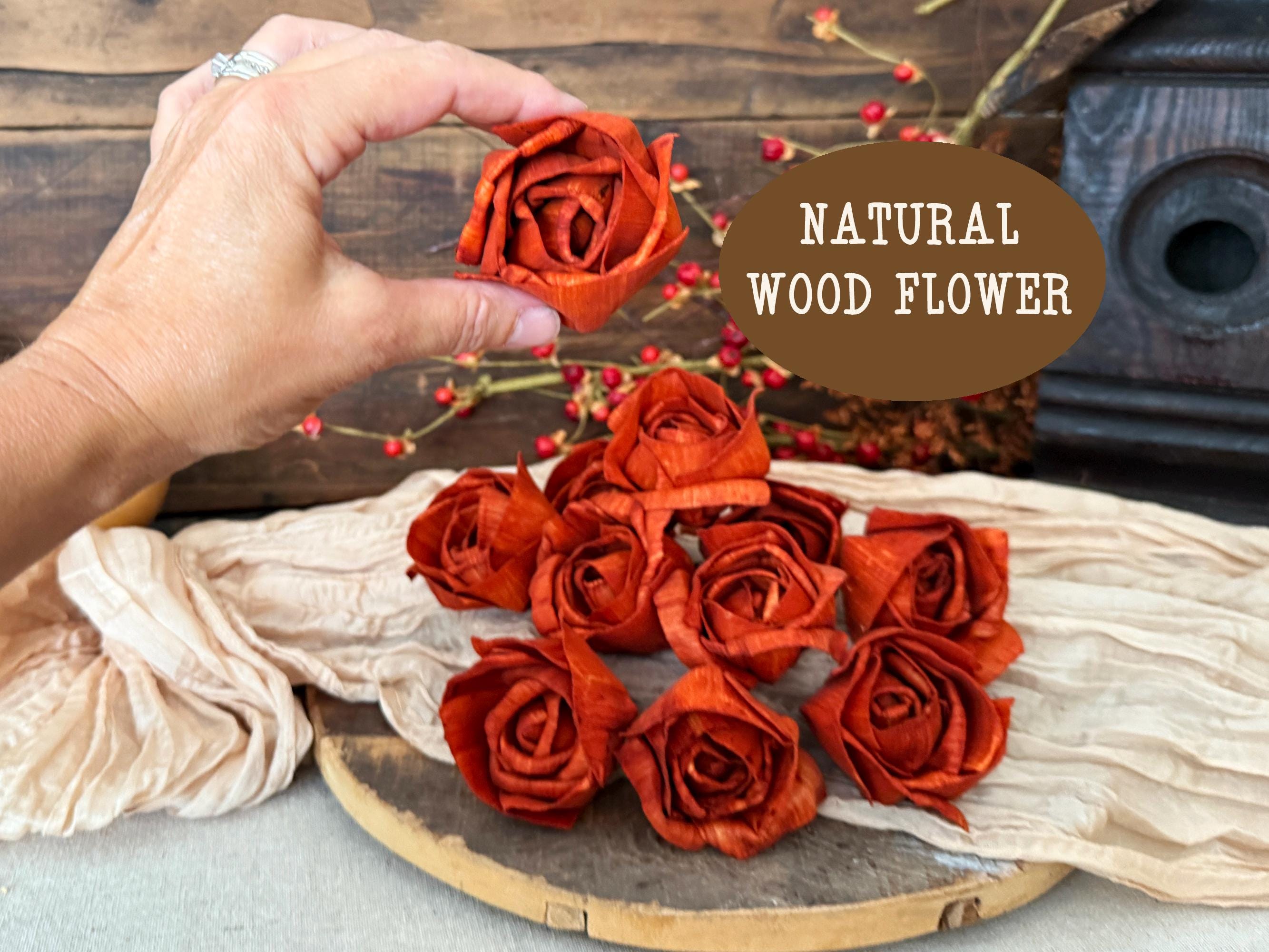 Orange wood flowers on a wooden surface with a hand holding one flower, on a rustic background.