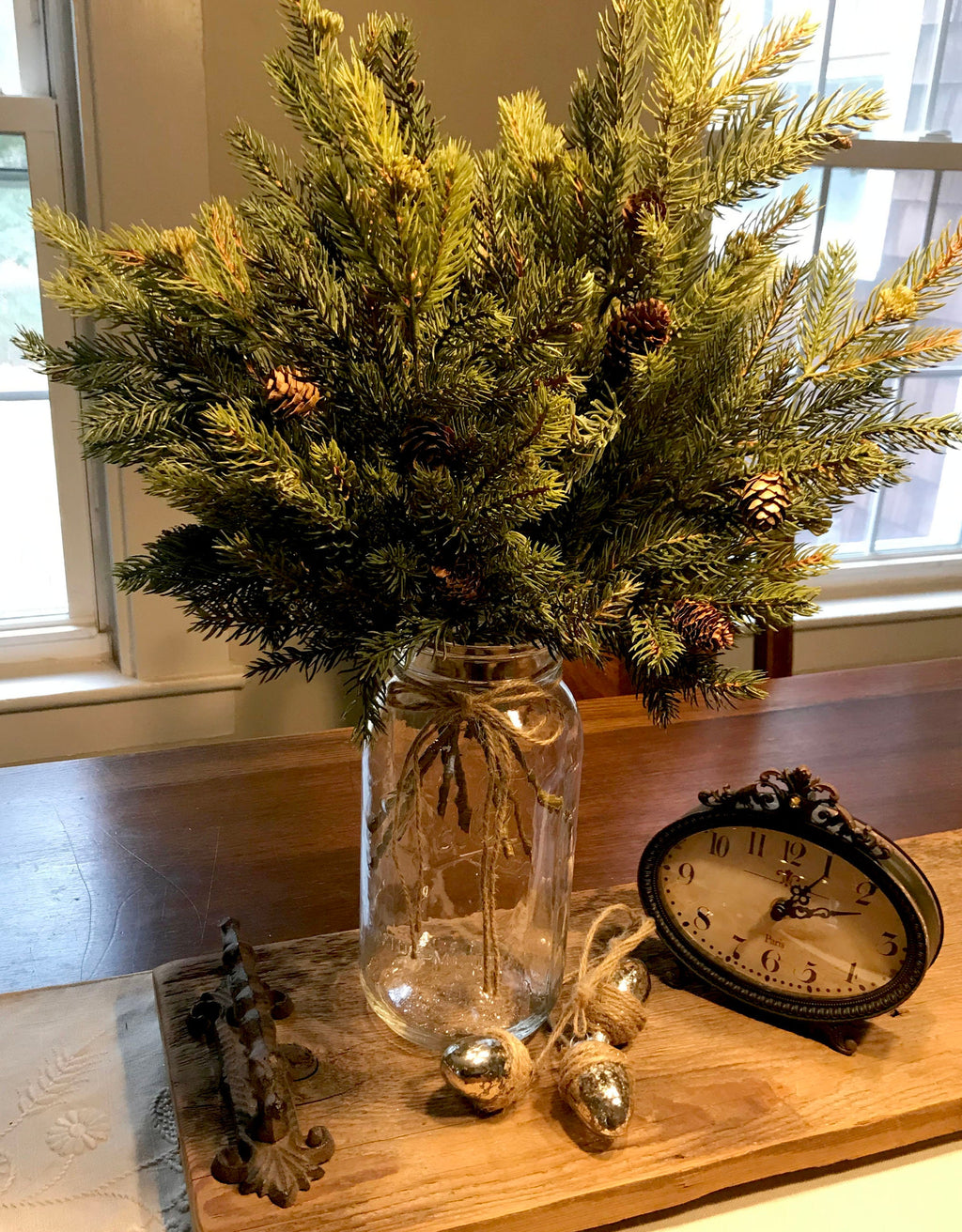 Decorative arrangement of greenery in a vase on a wooden surface with a clock and decorative items.