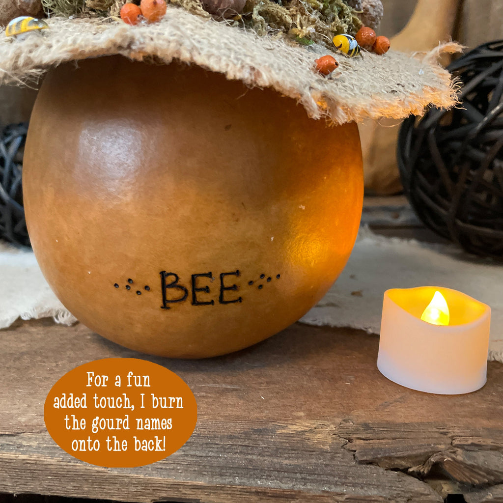 Decorative gourd with 'BEE' burned onto it, surrounded by a candle and natural elements.