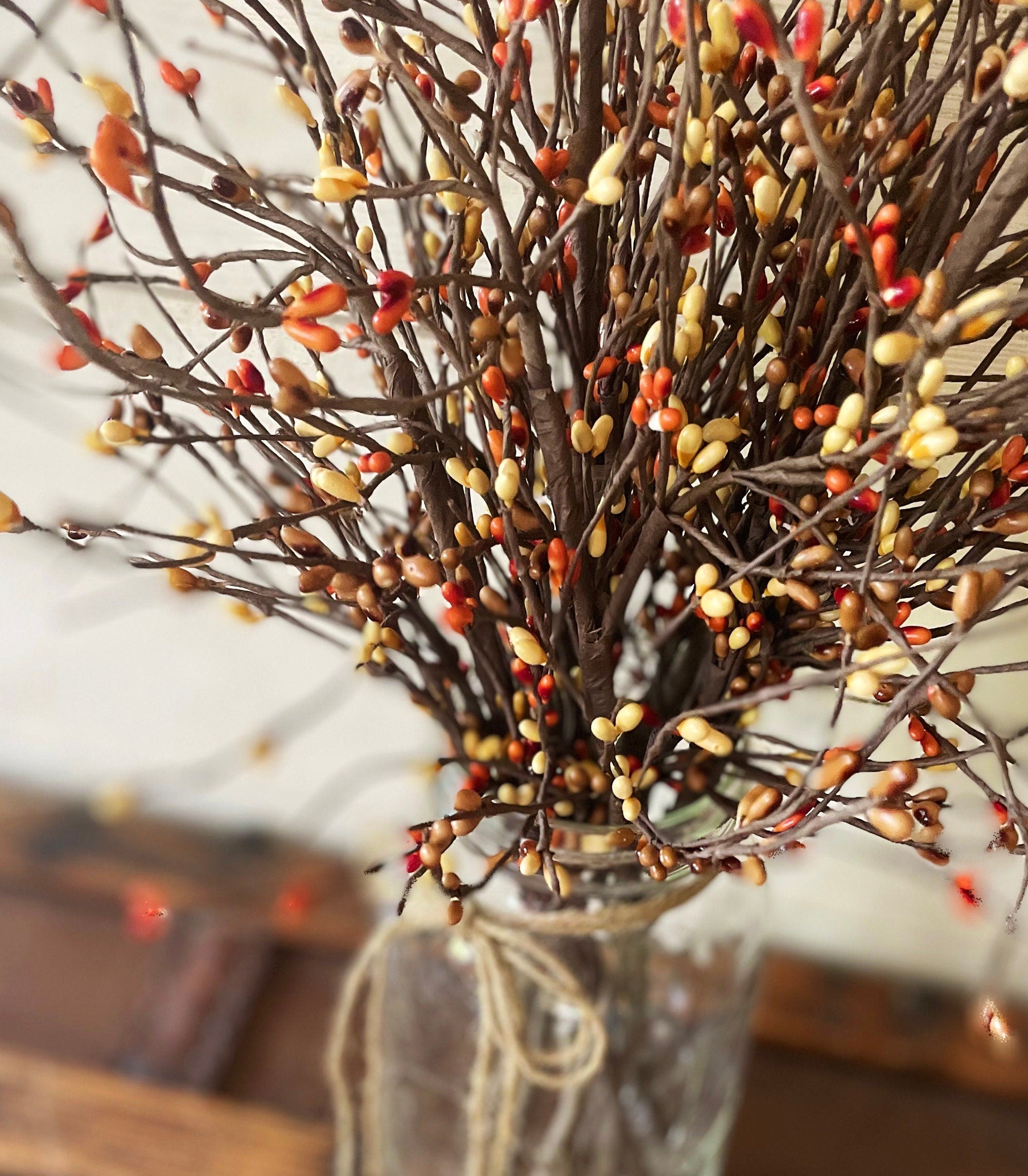 Decorative arrangement of branches with berries in a clear vase on a wooden surface.