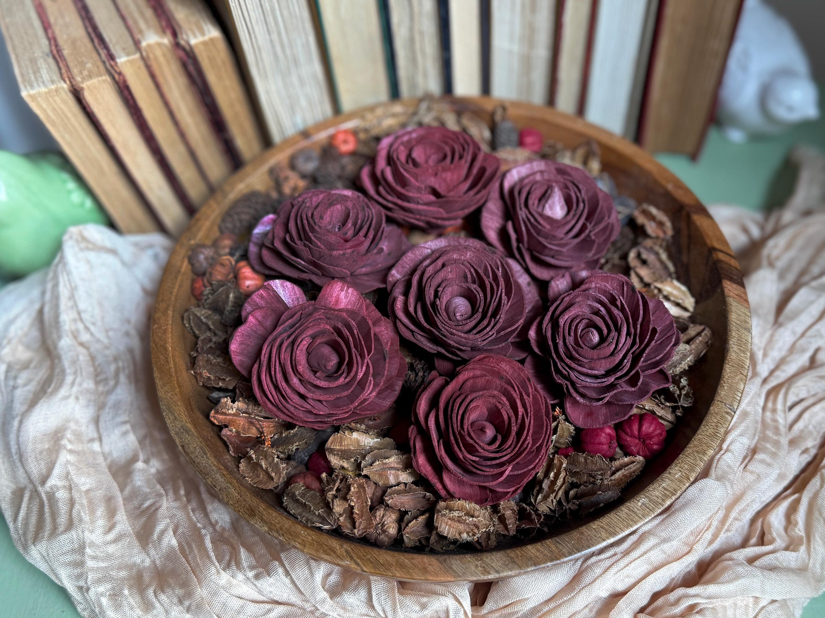 Wooden bowl filled with wood purple flowers on a textured surface with books in the background.