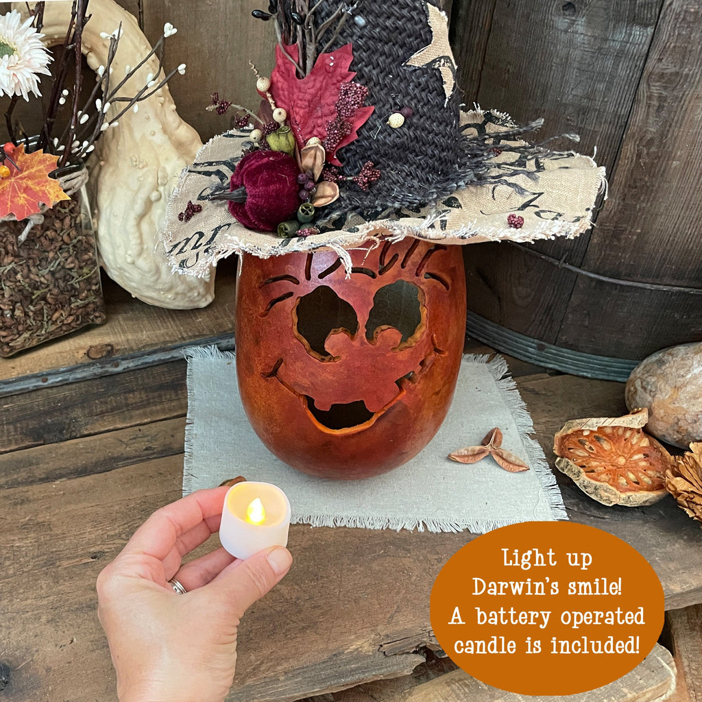 Decorative pumpkin with carved face, lit candle, and autumn leaves on a wooden surface.