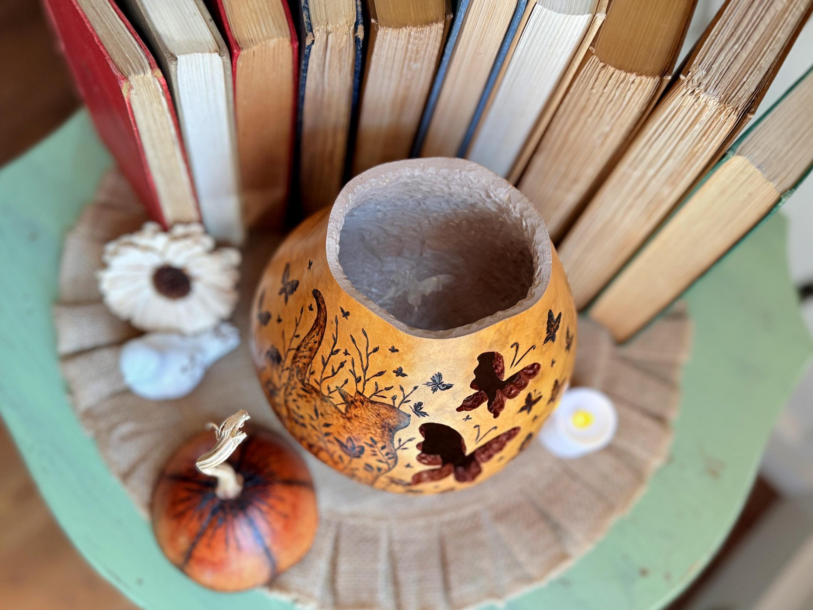 Decorative pumpkin with butterfly designs on a green surface with books in the background