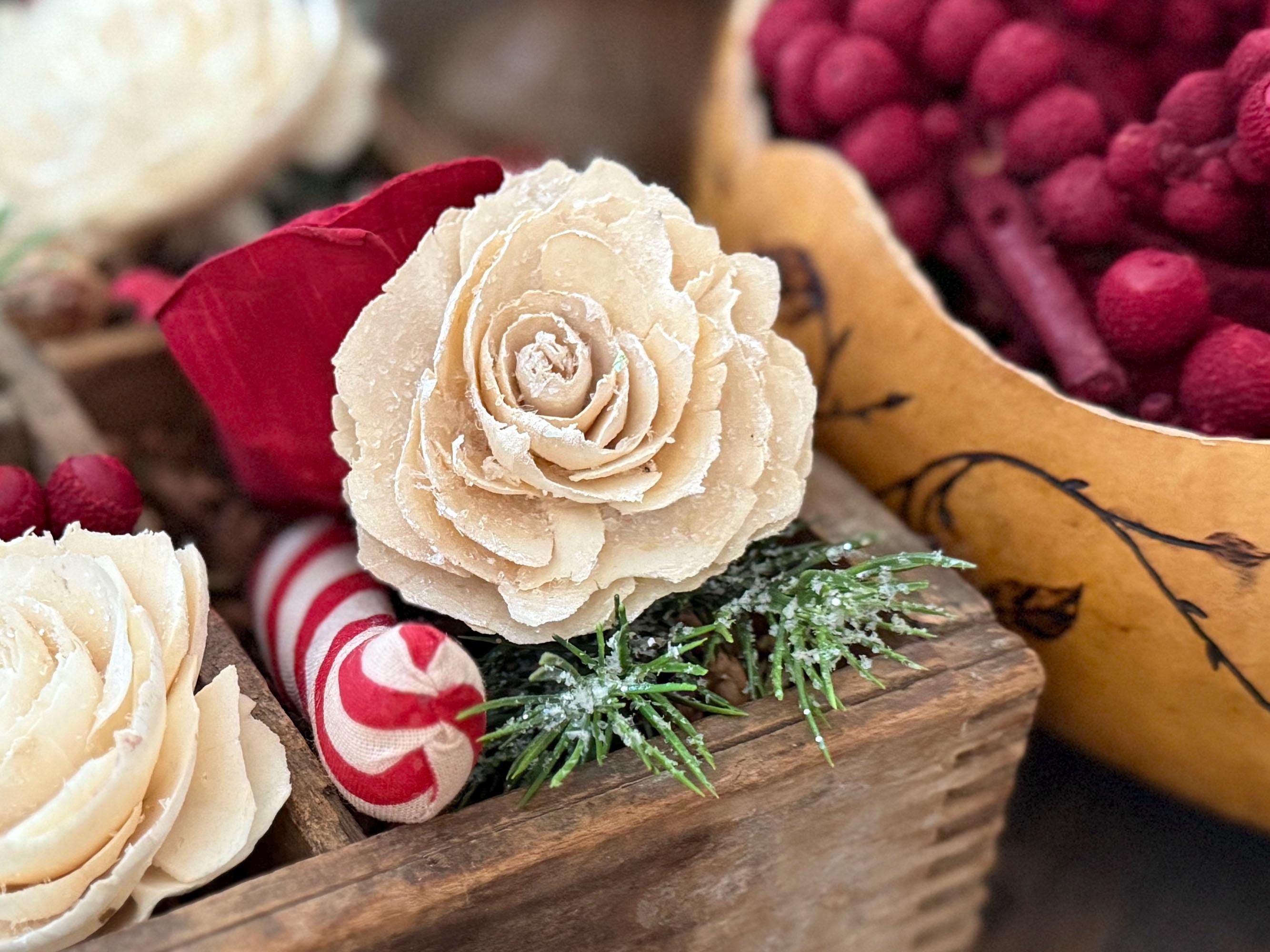 Decorative arrangement with beige flowers, red berries, and candy canes on a wooden surface.