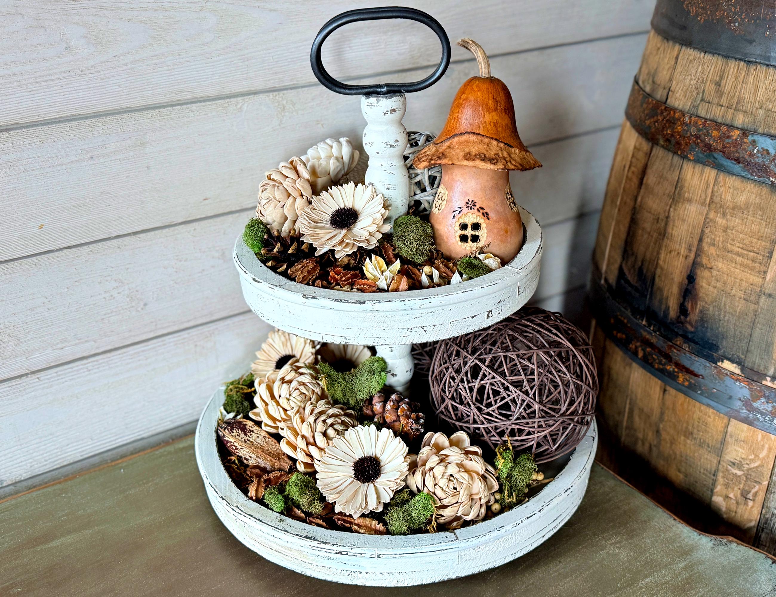 Two-tiered decorative stand with autumn-themed items including pumpkins and gourds against a wooden background.