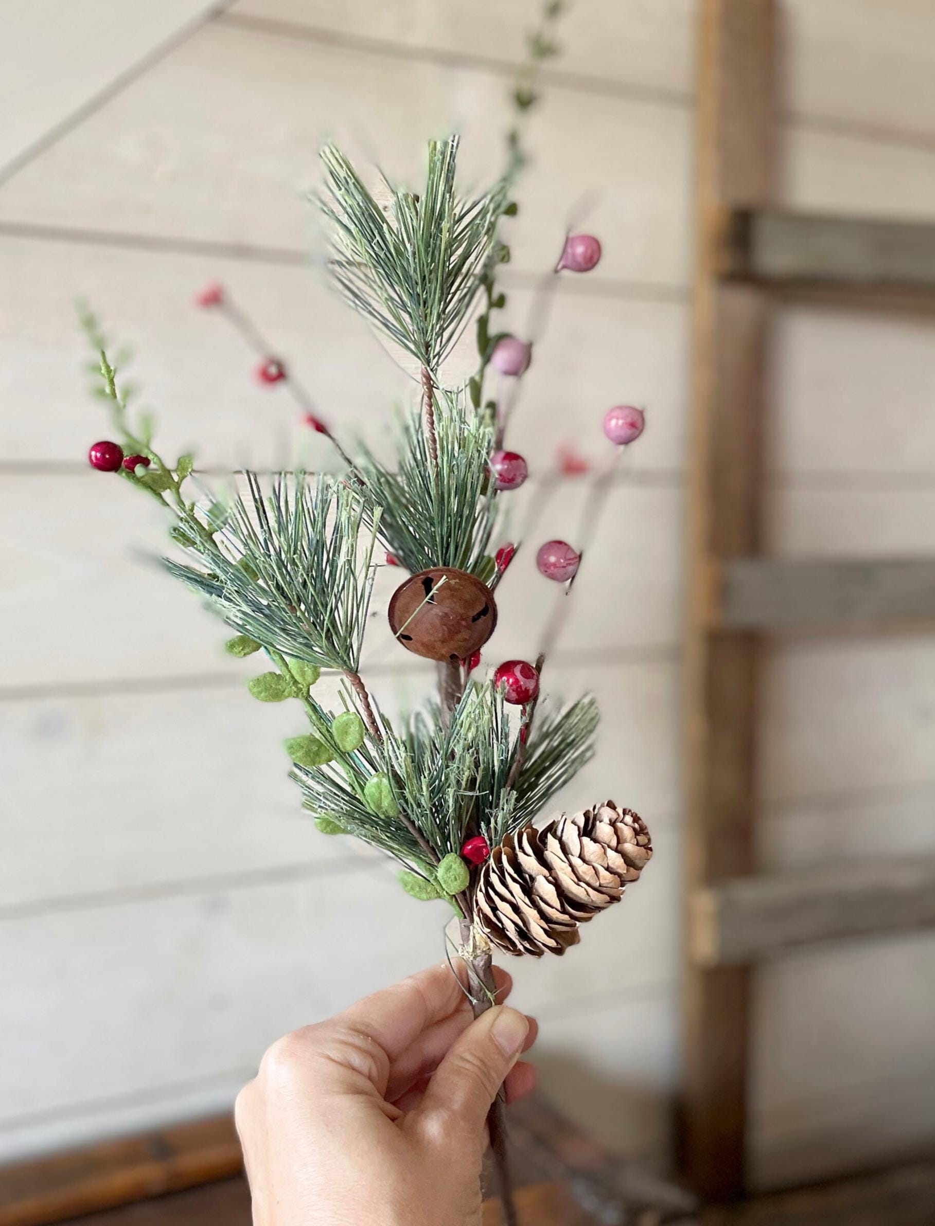 Hand holding a small arrangement of greenery, pinecones, and berries against a wooden background