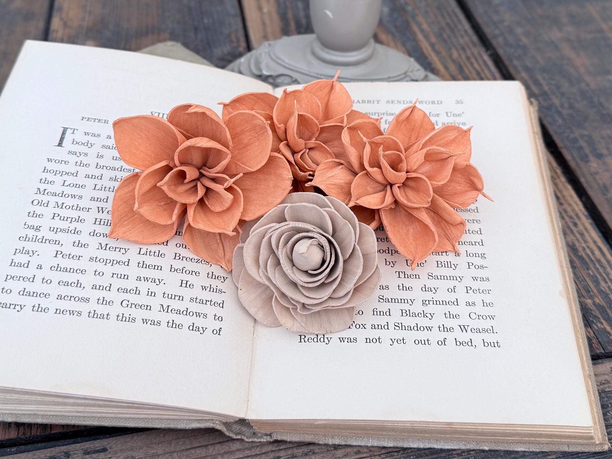 Three wood flowers in peach and gray colors on an open book.