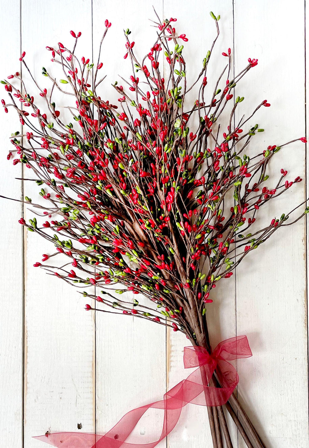 Bouquet of red and green branches with a pink ribbon on a white wooden background