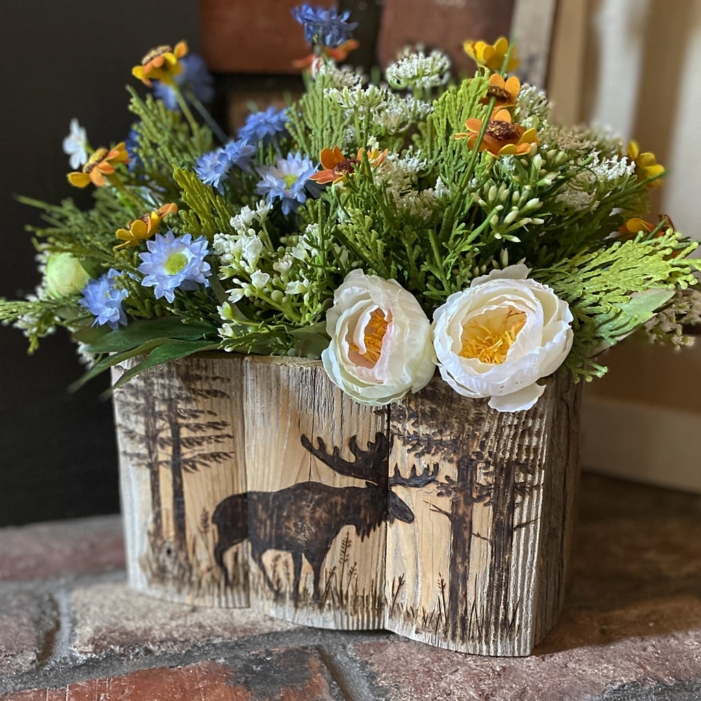 Floral arrangement in a wooden box with a moose design on a stone surface.