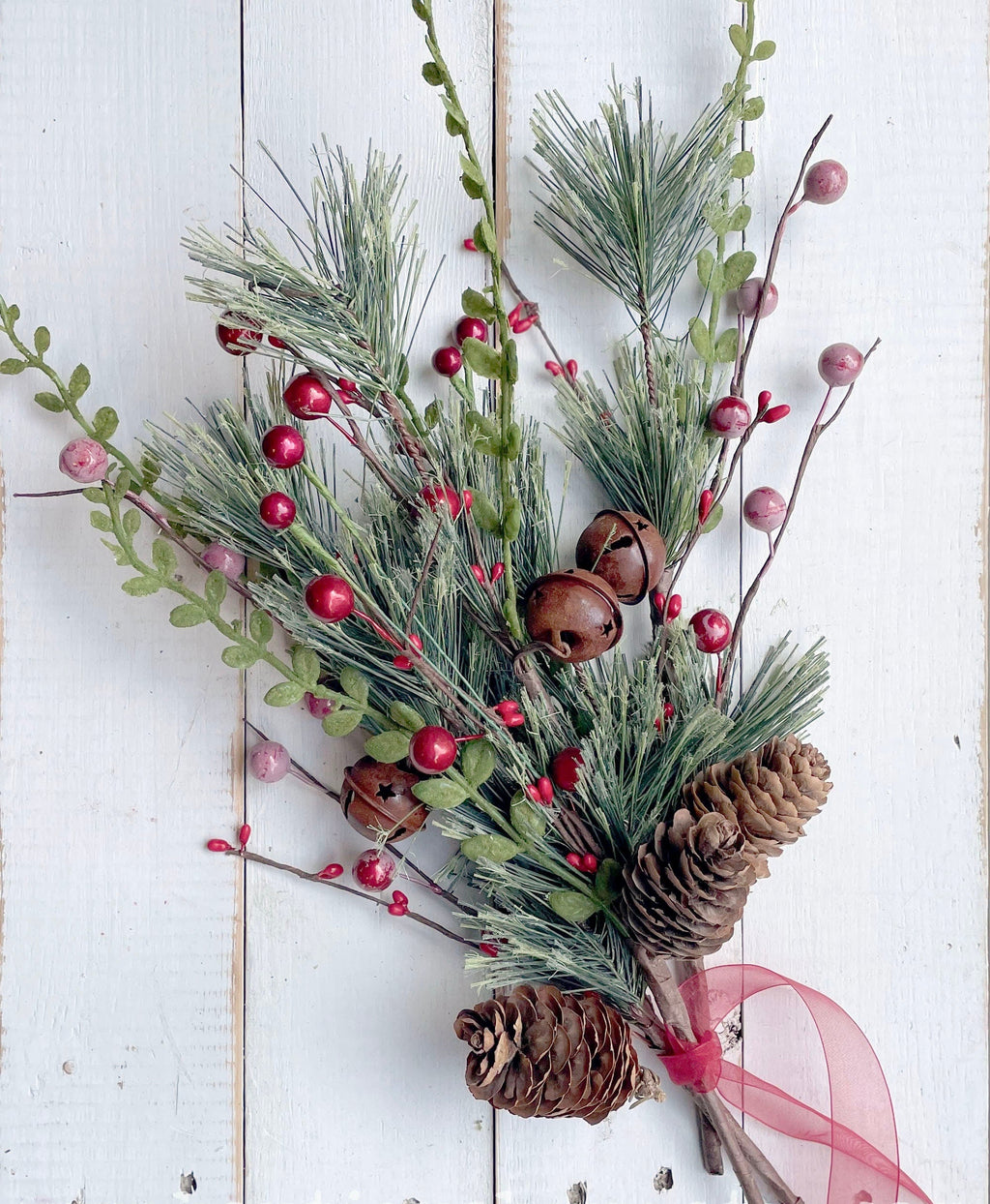 Decorative arrangement of greenery, pinecones, and red berries on a white wooden background.