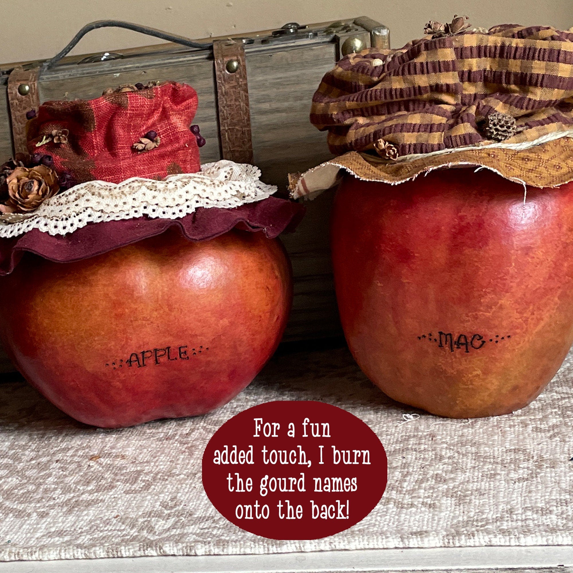 Decorative gourds with names burned onto them, placed on a textured surface with a suitcase in the background.