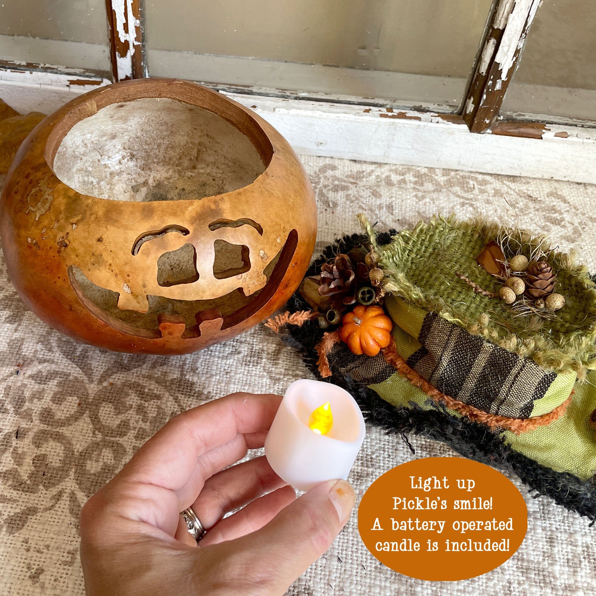 Hand holding a battery-operated candle next to a decorative pumpkin lantern on a rustic surface.
