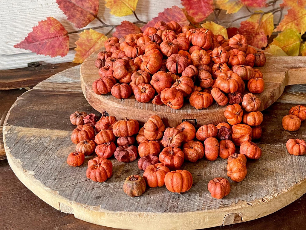 Stack of small pumpkins on a wooden surface with autumn leaves in the background