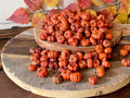 Stack of small pumpkins on a wooden surface with autumn leaves in the background