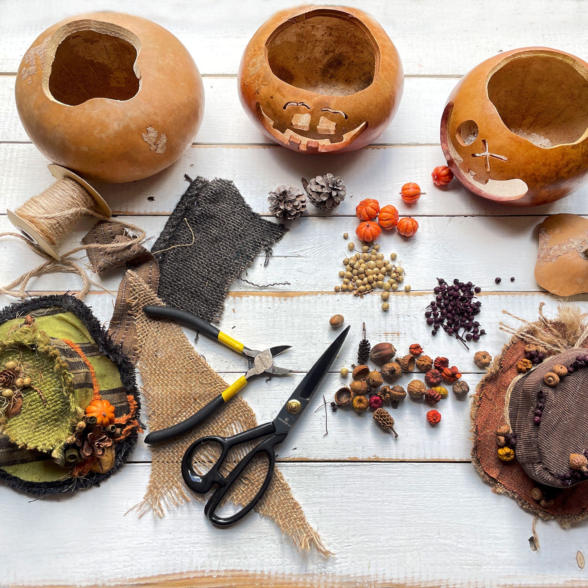 Gourds being carved into jack-o'-lanterns with carving tools and decorative items on a wooden surface.