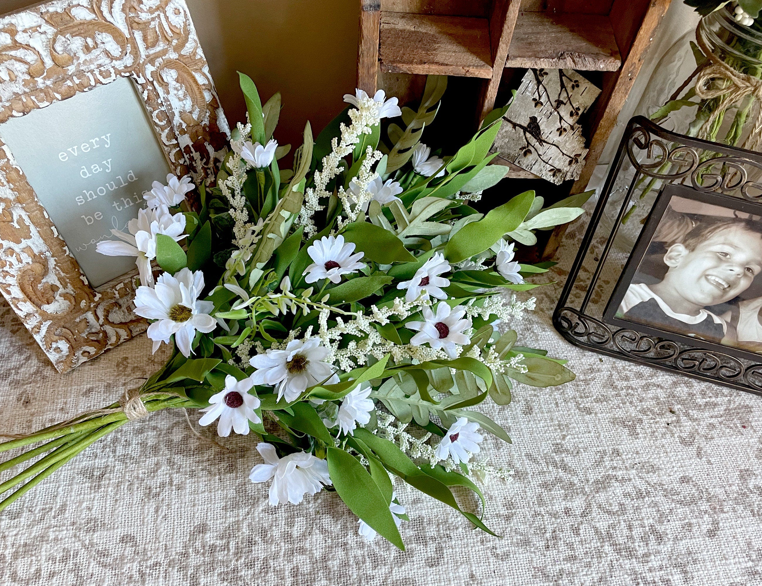 Bouquet of white flowers with green leaves on a textured surface with decorative frames.
