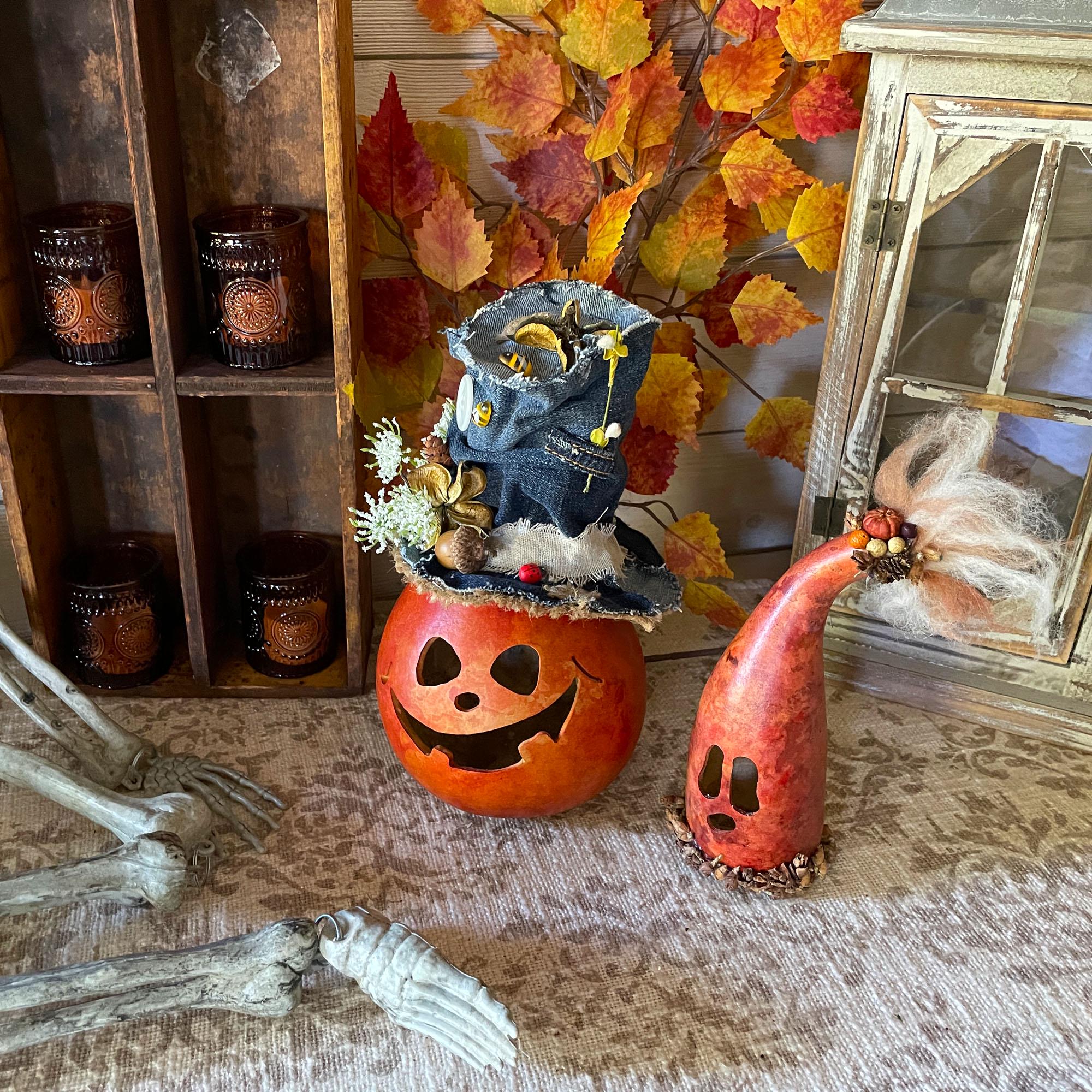 Halloween-themed decor with a jack-o'-lantern, gnomes, and skeleton hands on a textured surface.