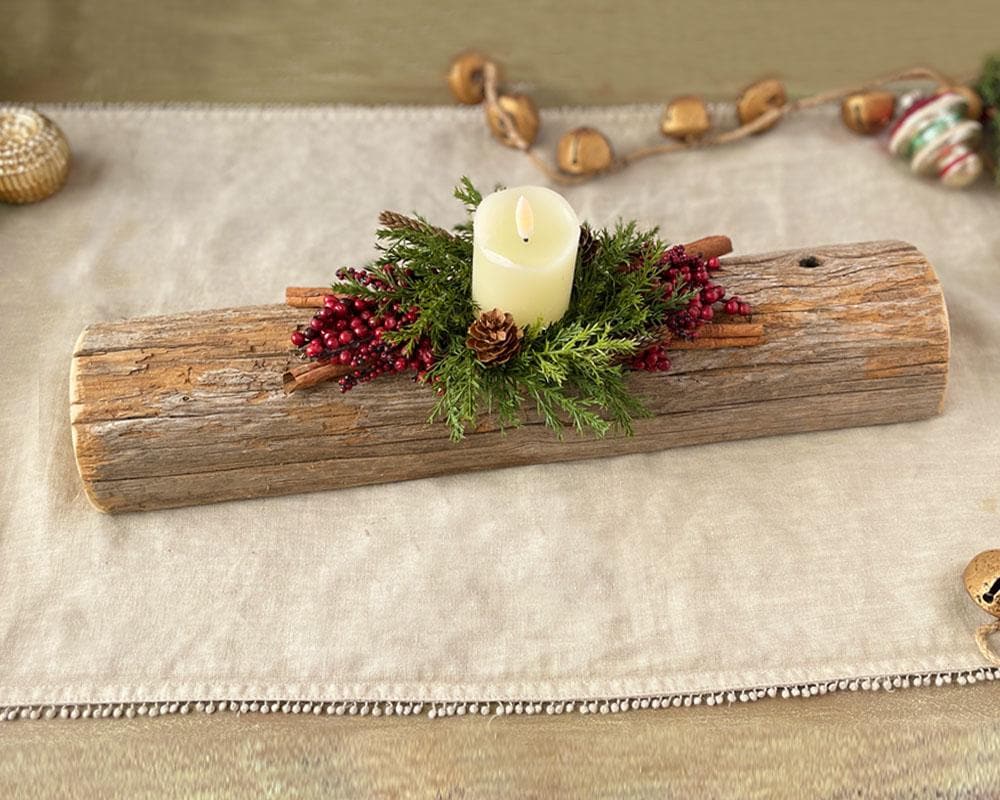 Decorative yule log with a candle, pine branches, and berries on a textured surface.