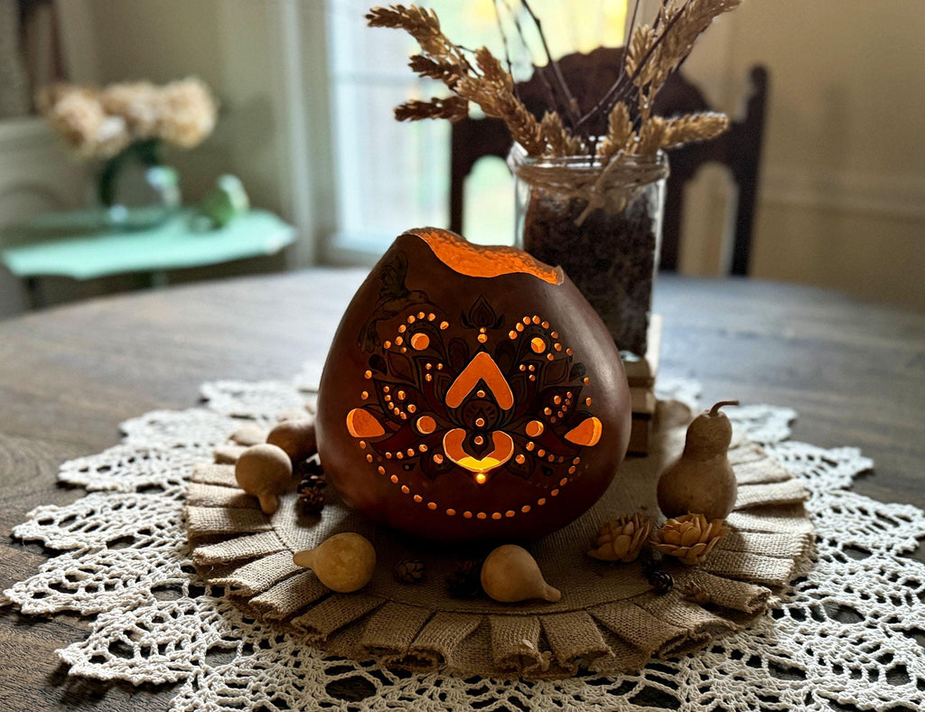 Decorative gourd luminary centerpiece on a table with a doily and small gourds.