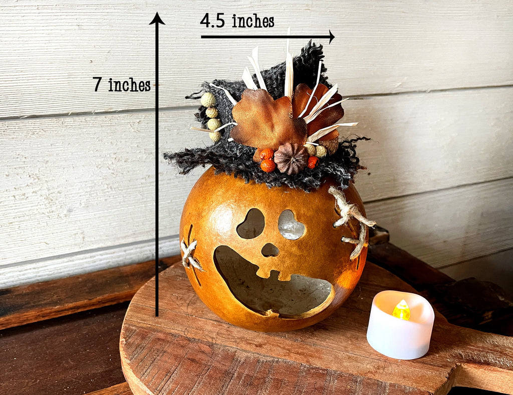 Decorative pumpkin with a carved face on a wooden surface, with measurements indicated.