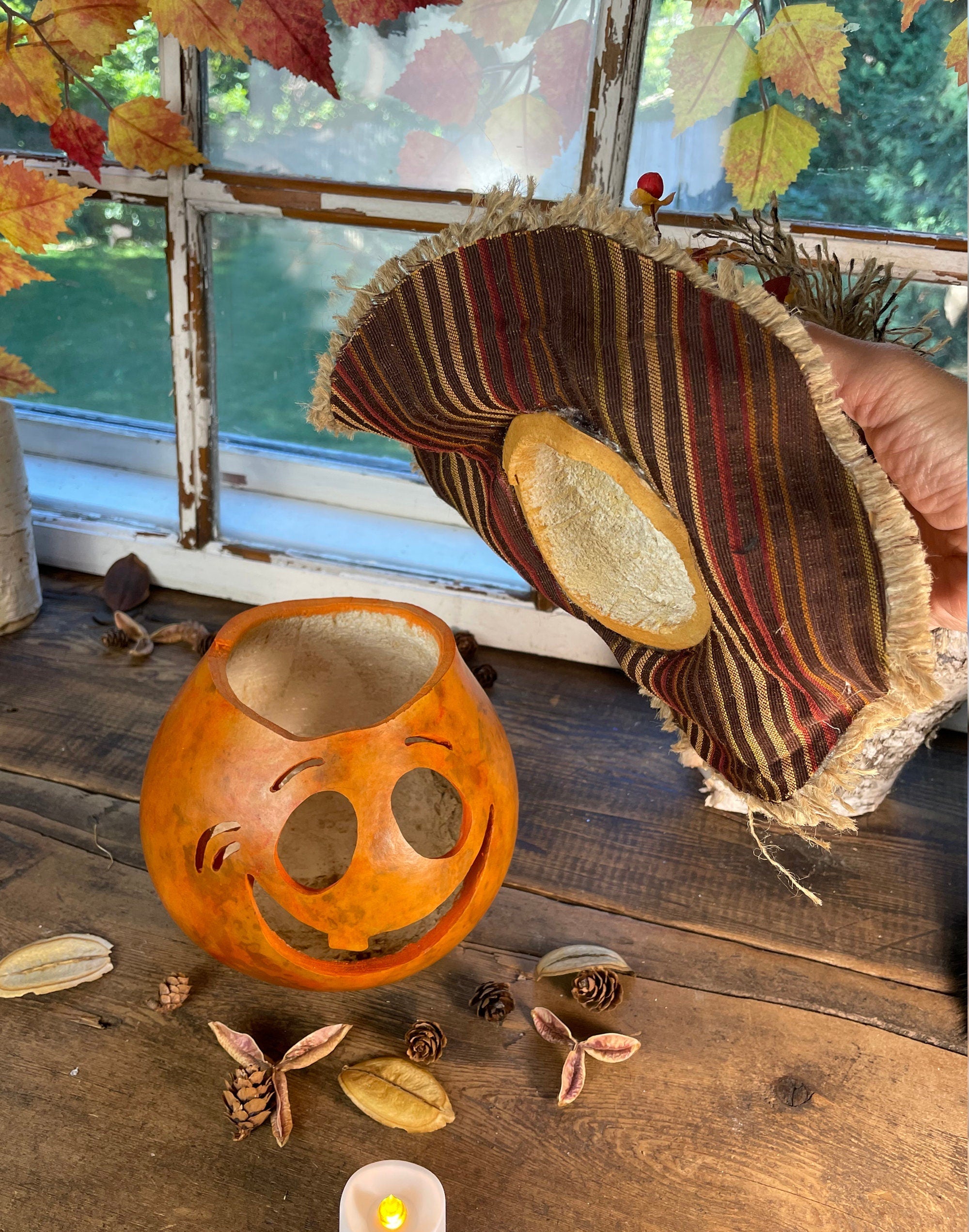 Decorative lantern and woven basket on a wooden surface with autumn leaves and pinecones.