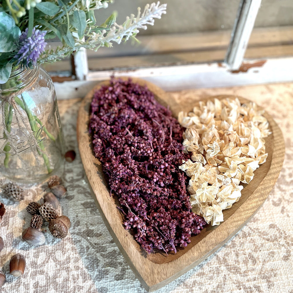 Wooden heart-shaped dish with dried flowers on a textured surface