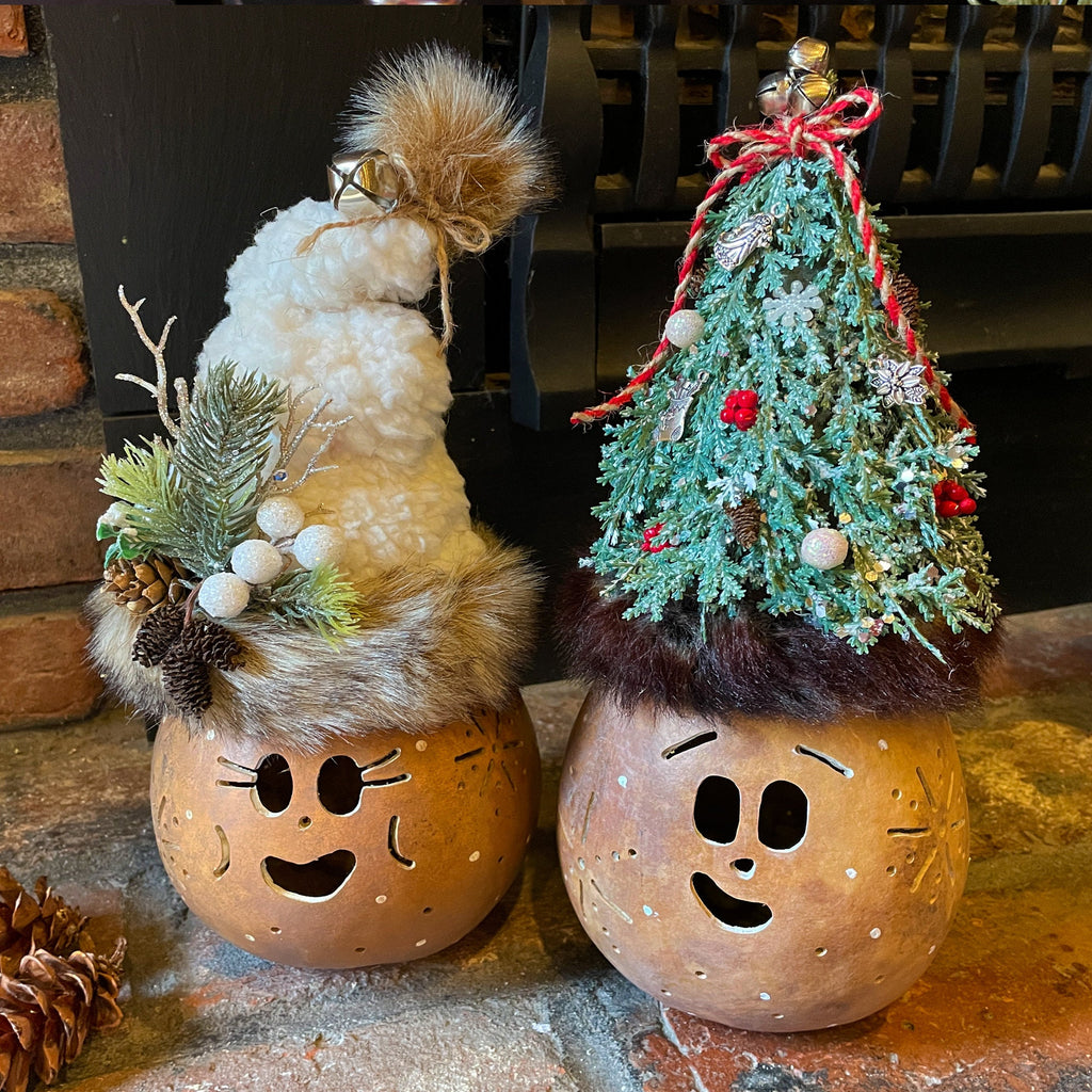 Two decorative gourds with face designs and Christmas tree topiaries on a stone surface.