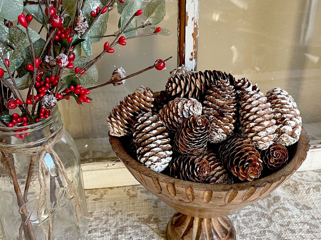 Decorative bowl with pinecones next to a jar with red berries on a textured surface.