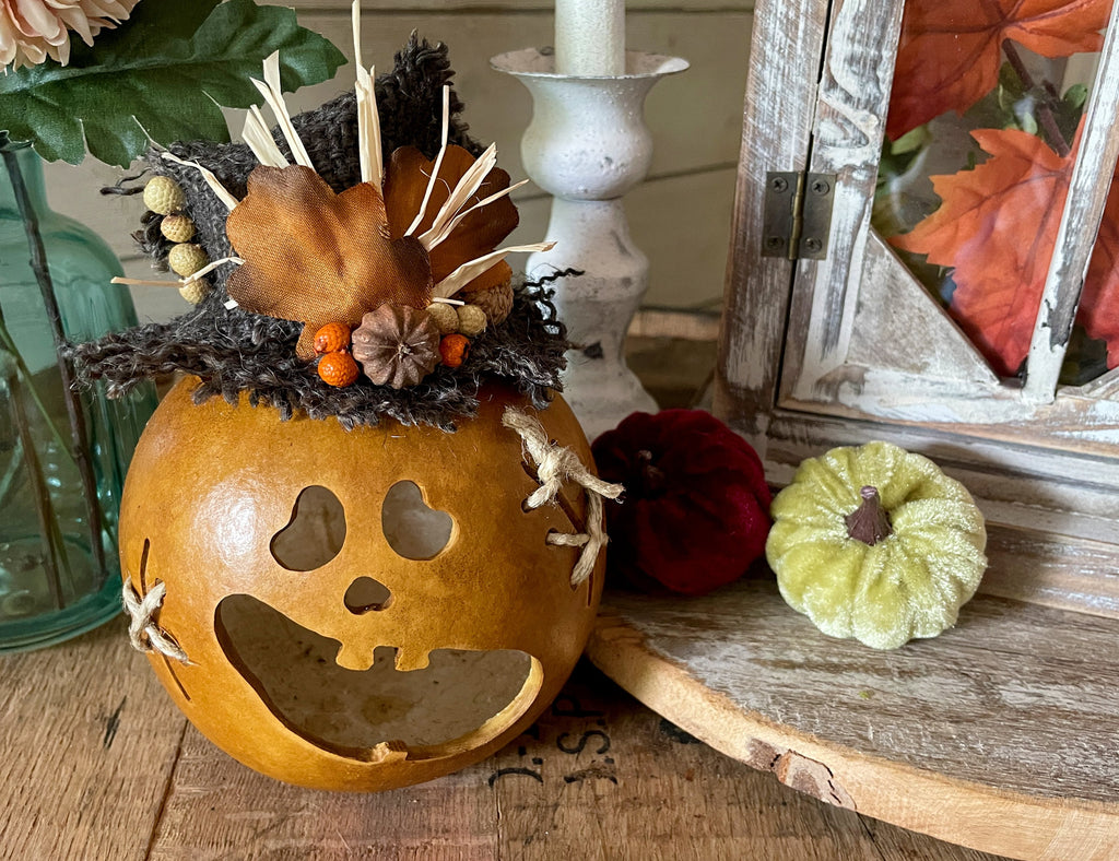 Decorative pumpkin with carved face on a wooden surface, surrounded by autumn-themed items.