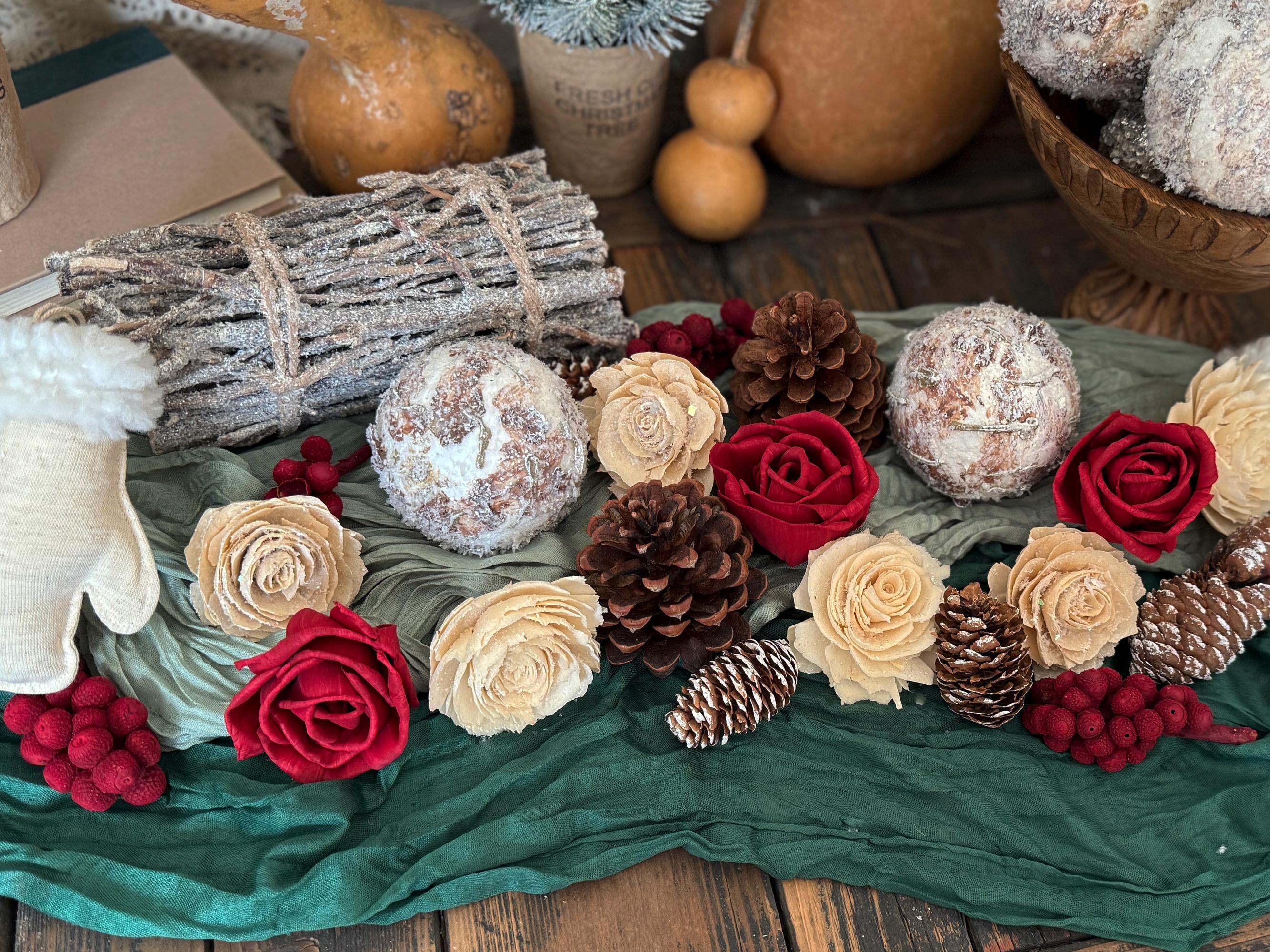 Decorative arrangement of flowers, pinecones, and logs on a green cloth with pumpkins in the background.