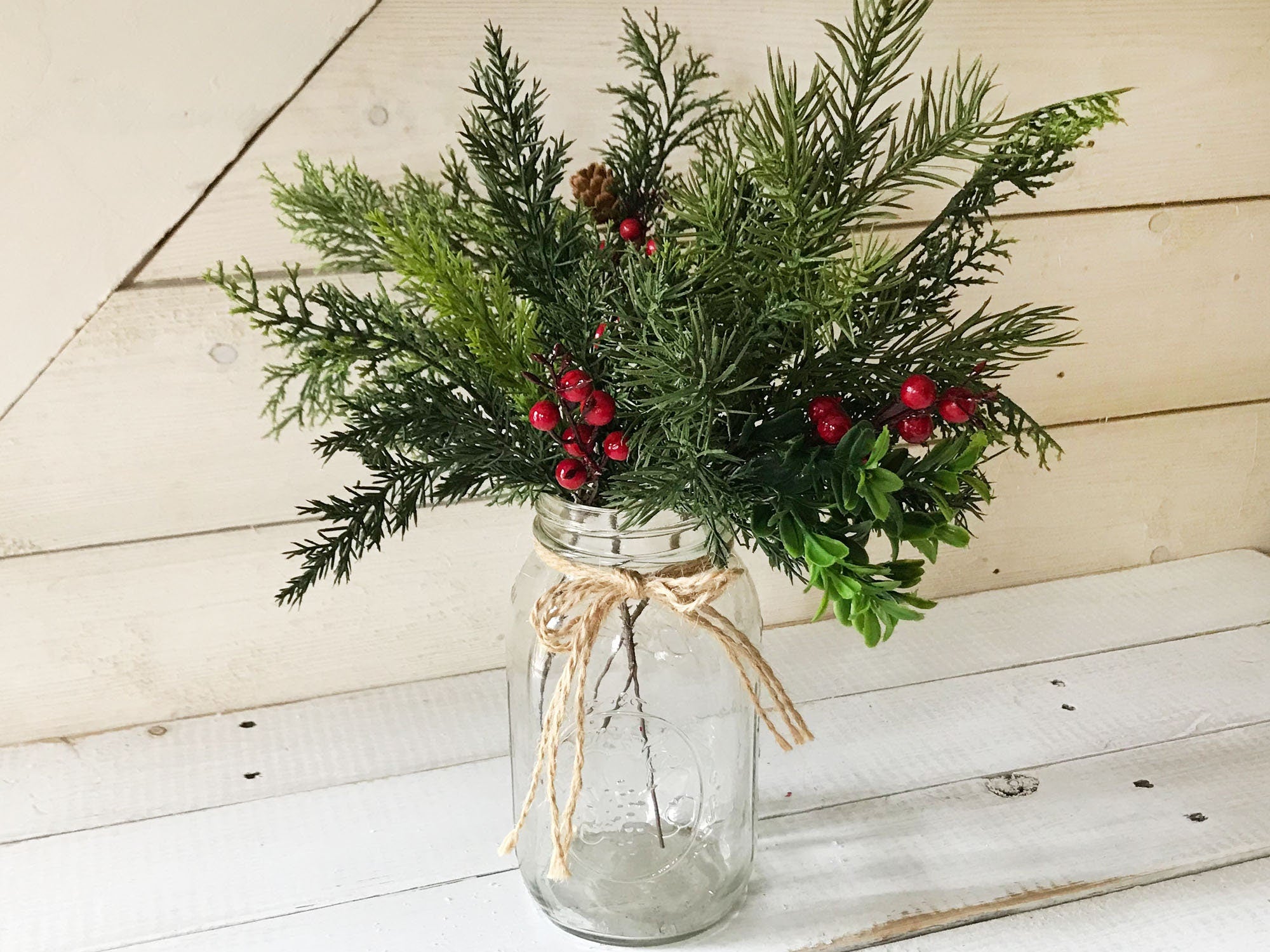 Bouquet of greenery and red berries in a glass jar on a wooden surface
