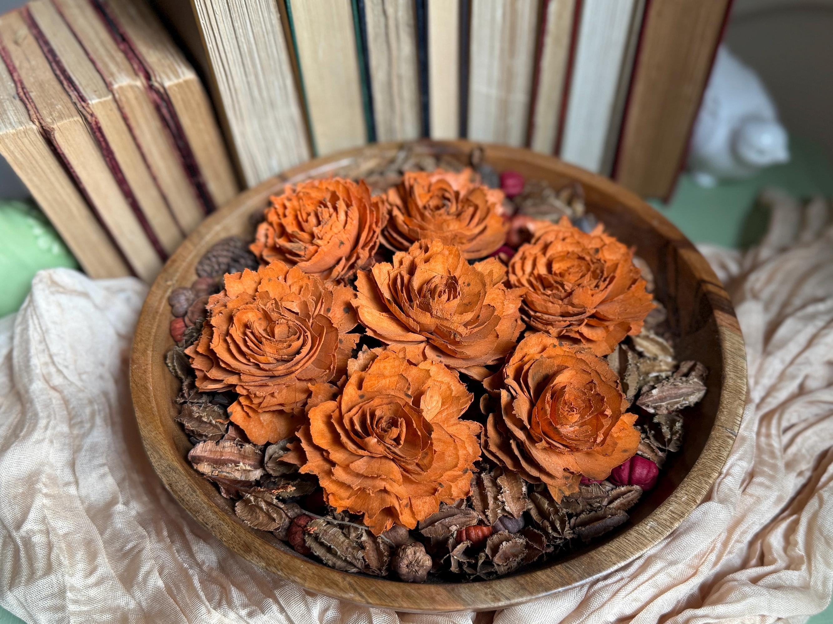 Wooden bowl with dried orange flowers and pinecones on a textured surface.