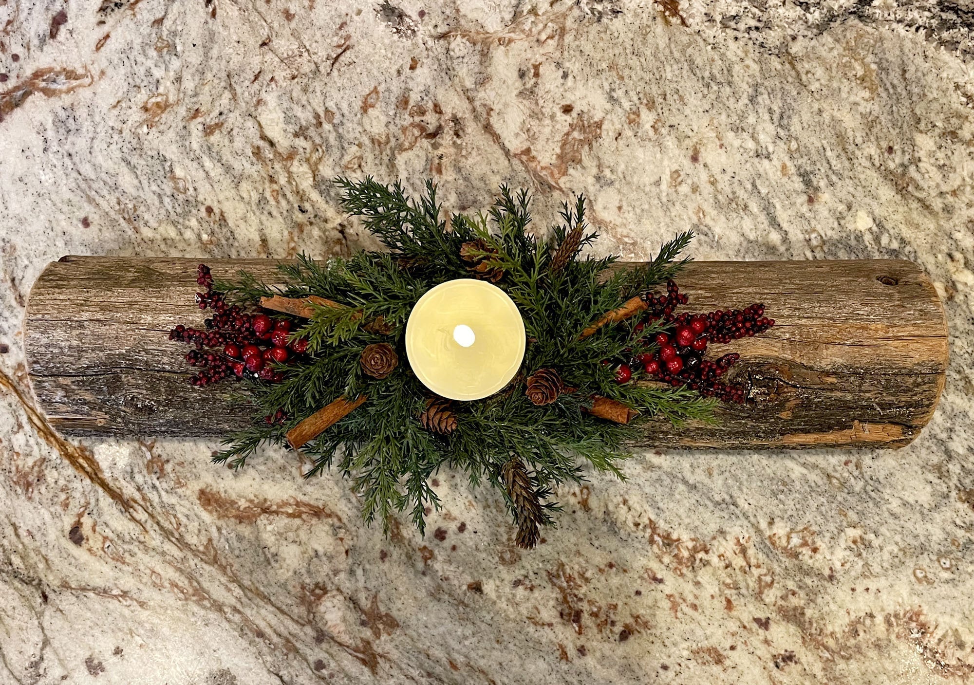 Decorative Christmas yule log candle holder with greenery and berries on a stone surface