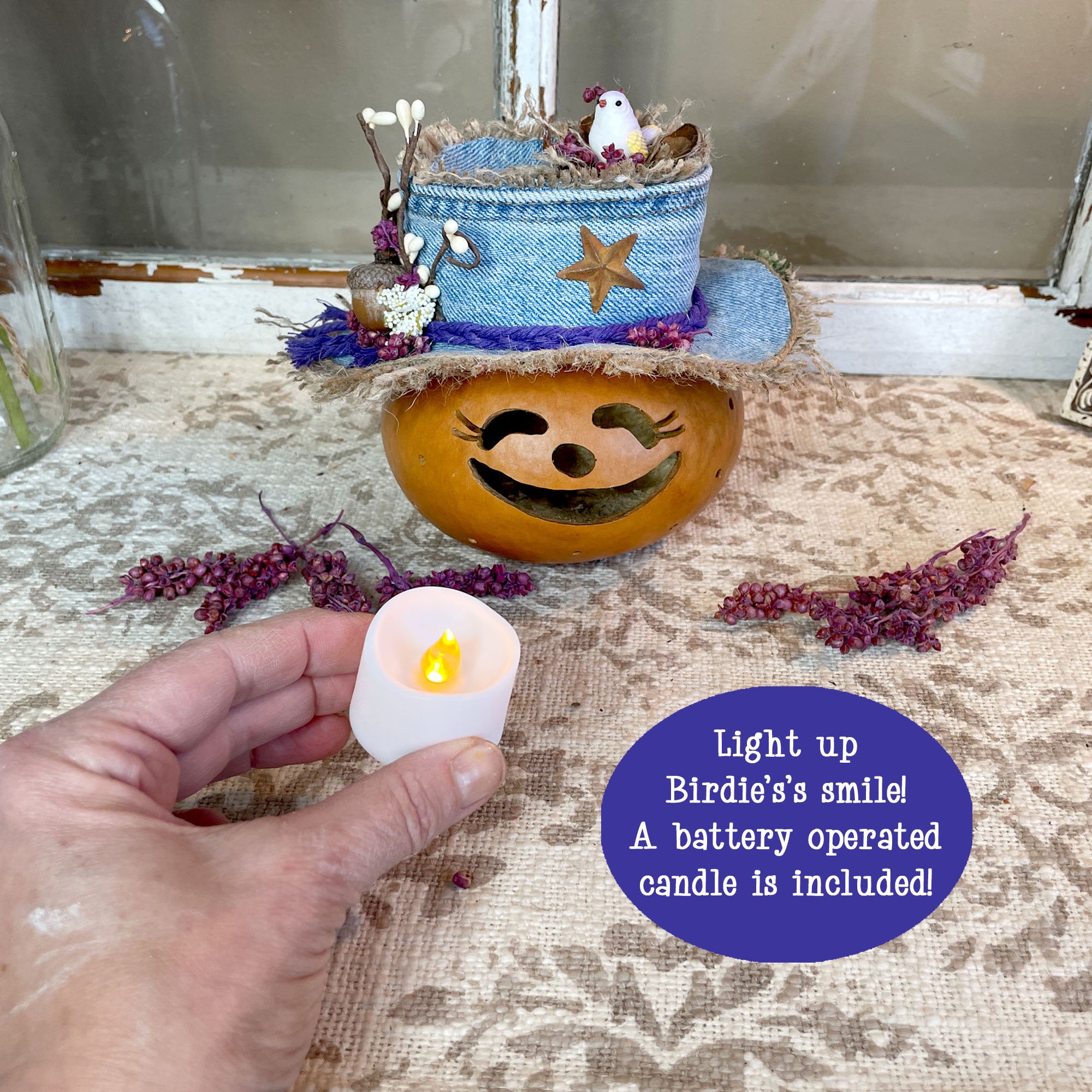 Decorative pumpkin with a hat and small bird figurine, lit by a battery-operated candle.