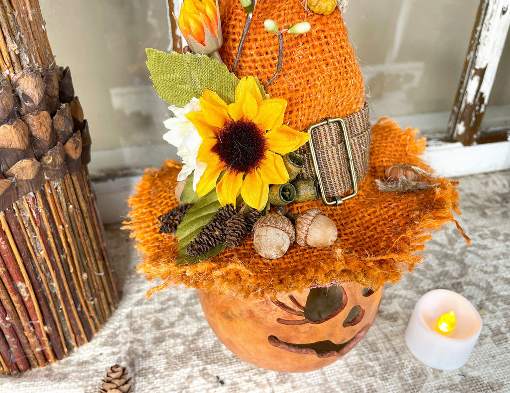 Decorative pumpkin with sunflower, acorns, and pinecones on a textured surface with a candle.