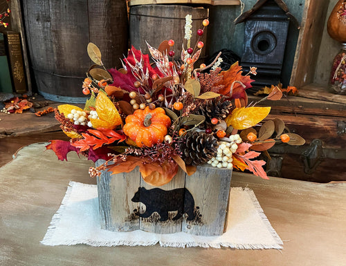 Autumnal floral arrangement in a wooden planter with a bear silhouette on a rustic wooden table.