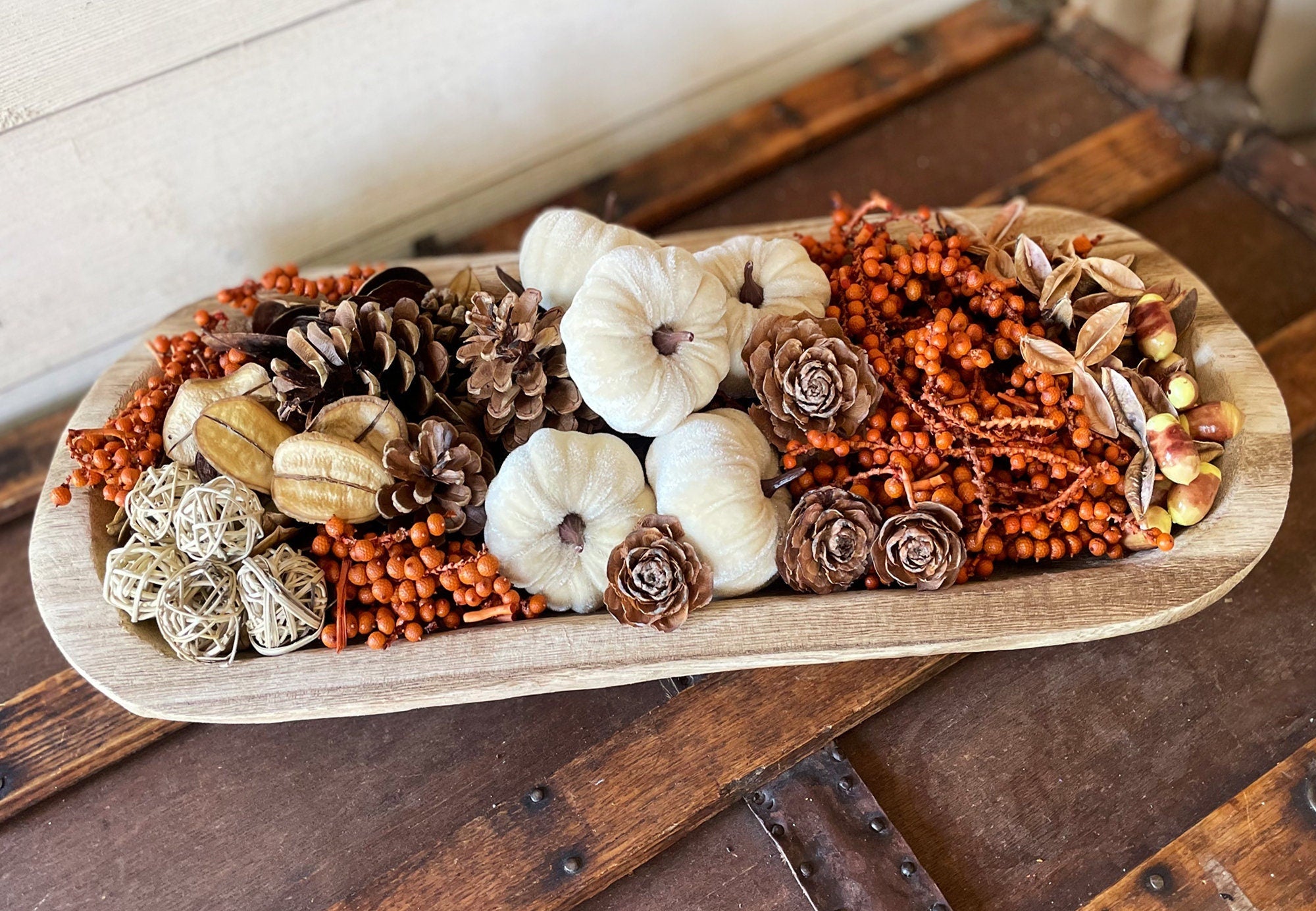 Decorative arrangement of pumpkins, pinecones, and berries on a wooden dough bowl with a rustic background.
