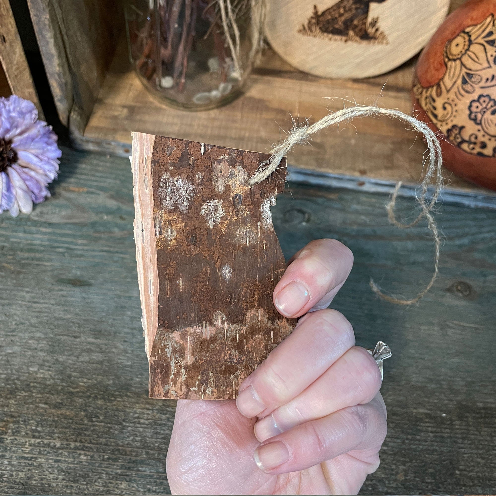 Hand holding a small wooden tag with a rustic texture on a wooden surface.