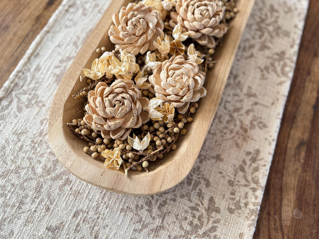 Wooden dough bowl filled with dried flowers and herbs on a textured fabric surface