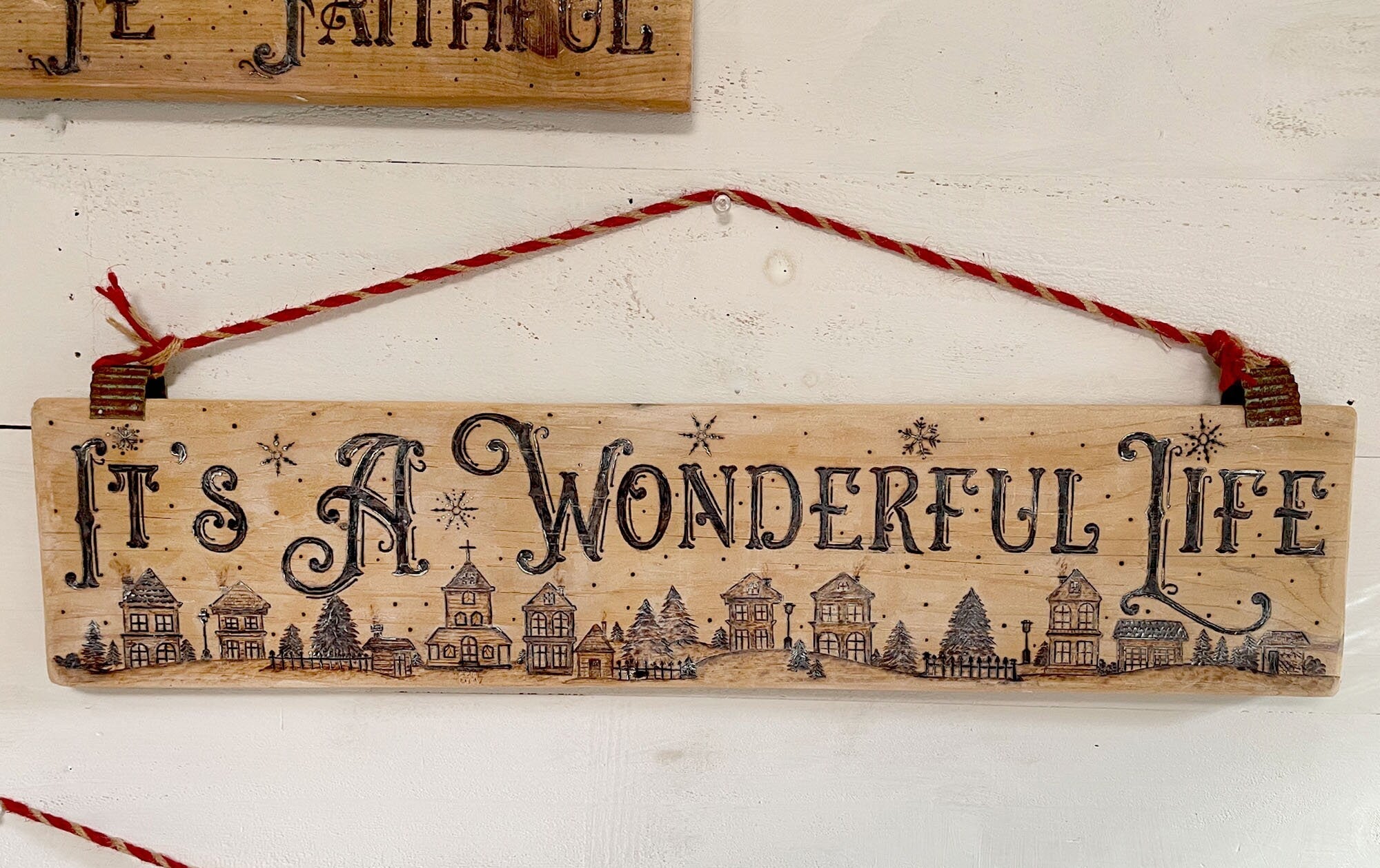 Wooden sign with 'It's a Wonderful Life' text and small illustrations, hanging on a white wall.