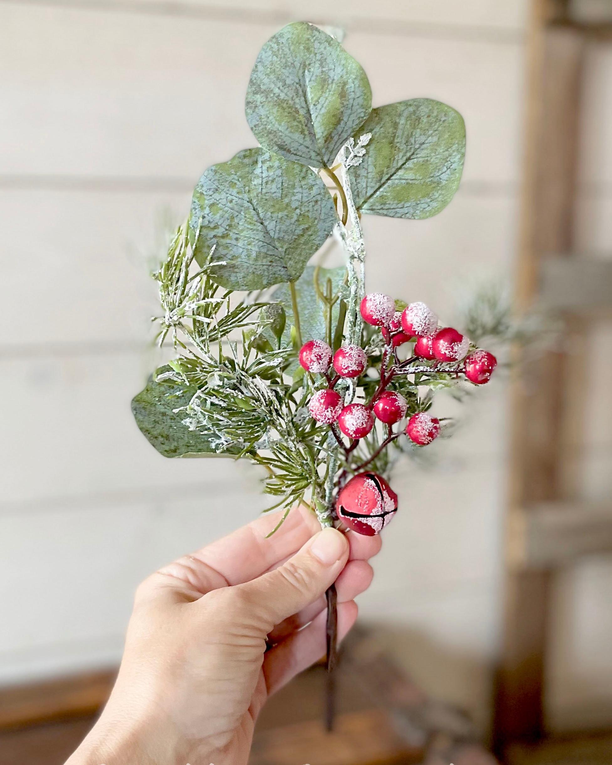 Hand holding a small bouquet of green leaves and red berries against a neutral background
