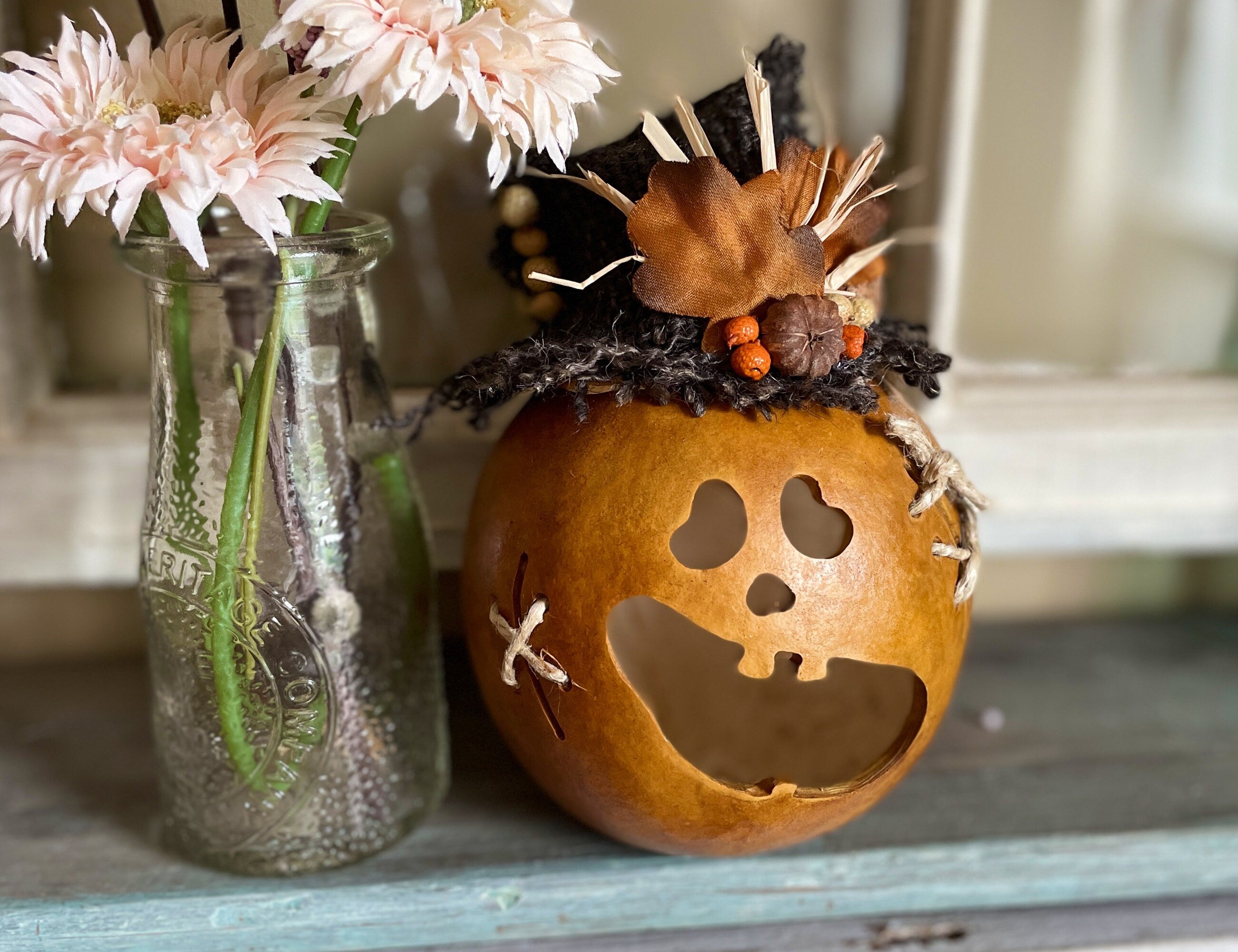 Decorative pumpkin with a face cutout next to a vase with flowers on a wooden surface.