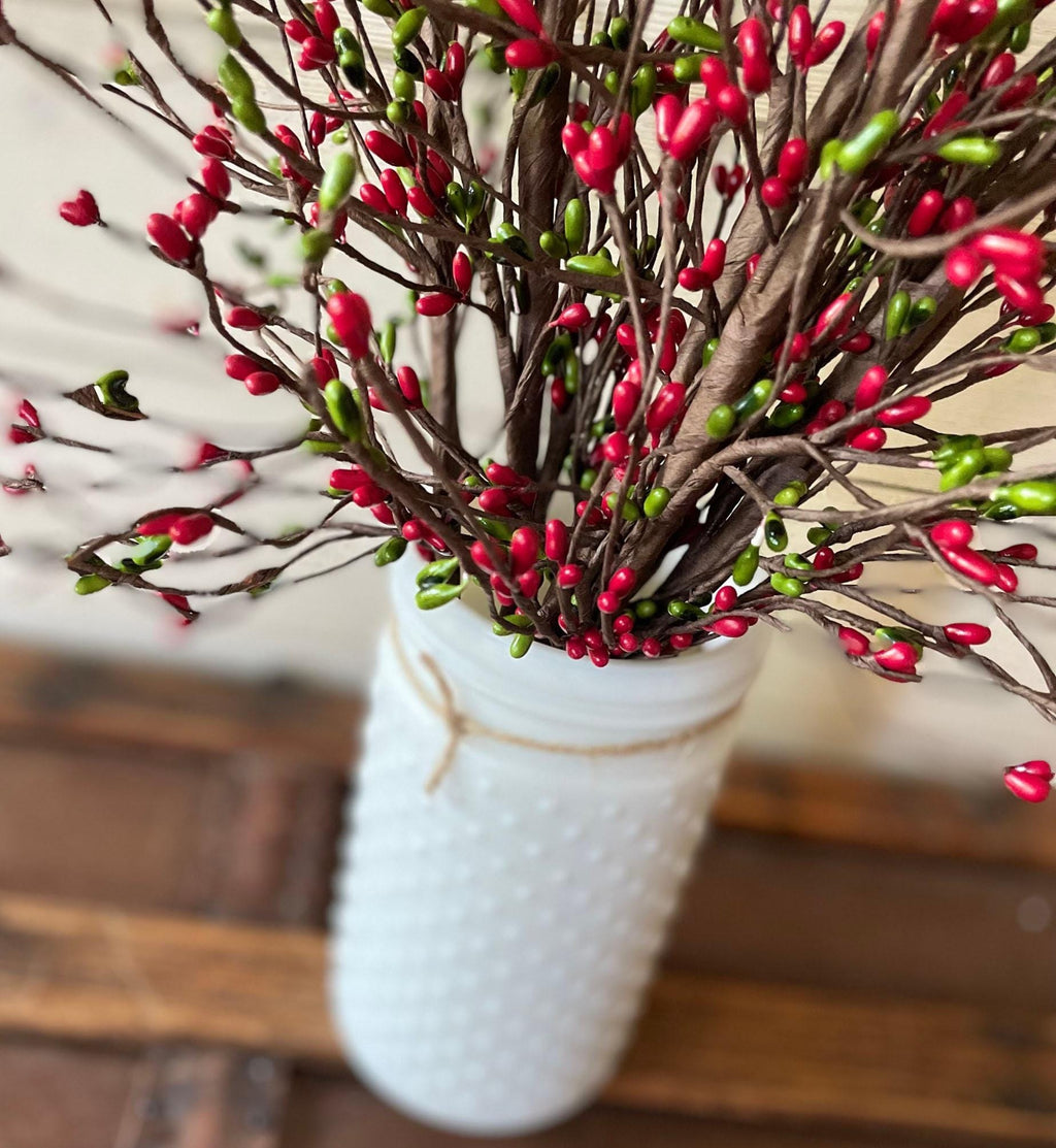 Bouquet of red and green artificial flowers in a white textured vase on a wooden surface.